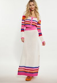 Megztas dviejų dalių komplektas, kuriame yra daugiakampės juostelės trumpas kardiganas ir baltos ilgis sijonas su rožine liemens juosta ir šonine skeltimi.