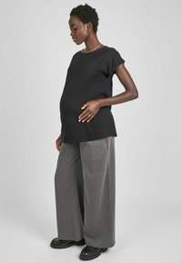 Un top scurt negru cu mâneci scurte, asociat cu pantaloni lati gri și încălțăminte cu platformă neagră. Texturile textile sunt netede și bine croite.