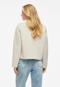 Giacca trapuntata crema con design cropped, maniche lunghe e una texture morbida, abbinata a jeans azzurri chiari in una vestibilità comoda.