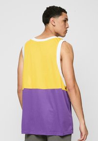 Fargeblokkert ermel�øs jersey med en gul øvre del og en lilla nedre del, laget av mesh-materiale med hvit trim langs halslinjen.