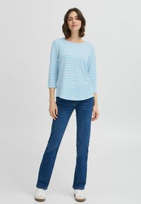 Maglietta a maniche lunghe a righe blu e bianche, colletto a girocollo, vestibilità rilassata, abbinata a jeans blu scuro e scarpe da ginnastica bianche. Tessuto di cotone morbido.