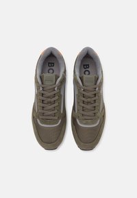 Sneakers atléticos verde-azeitona com uma mistura de materiais em malha e camurça, detalhes cinza e atacadores texturizados. Logótipo na língua e no calcanhar.