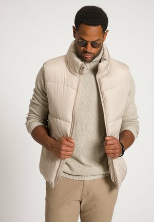 Chaleco acolchado beige con alto cuello, frente con cremallera y una textura suave, sobre un suéter gris claro. Seleccionado por su calidez y para superponer.