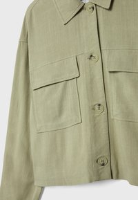 Jasnozielona kurtka zapinana na guziki o miękkiej fakturze, z dwoma kieszeniami na piersi i kołnierzykiem. Kwadratowy krój i luźny fason.