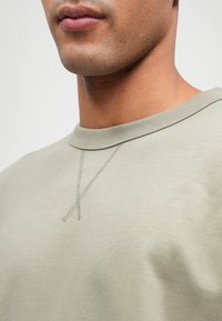 Světle olivově zelená mikina s kulatým výstřihem, která se vyznačuje jemnými švy a měkkou texturou. Navržena pro volný střih.