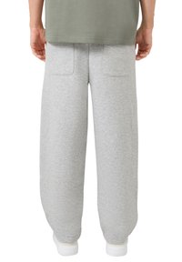Person, der helle graue Jogginghosen mit Gesäßtaschen, ein olivgrünes Shirt und weiße Sneakers trägt, von hinten gezeigt.