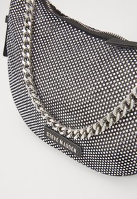 Black handbag with a textured surface of small silver studs, a silver chain strap, and a black zipper. Features a logo tag.