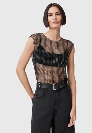 Top in rete nera con design trasparente e maniche corte, indossato sopra un canottiera nera aderente. Abbinato a pantaloni neri a vita alta e una cintura.