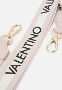 Cinghia accessoria Valentino realizzata in tessuto rosa chiaro con accenti del logo bianchi e neri, hardware in metallo dorato e dettaglio in pelle texturizzata.