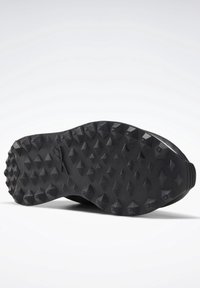 Semelle de chaussure noire avec des crampons en relief triangulaires et en forme de losange pour une meilleure adhérence sur diverses surfaces.