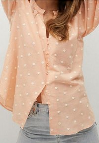 Perzikkleurig shirt met witte, textuurlijke stippen, knoopsluiting aan de voorkant, ontspannen pasvorm en een licht gebogen zoom. Zacht, lichtgewicht materiaal.
