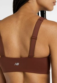 Brun behå med breda band och en slät, matt yta. Har en liten vit logotyp på baksidan. Fokus på baksidans design.