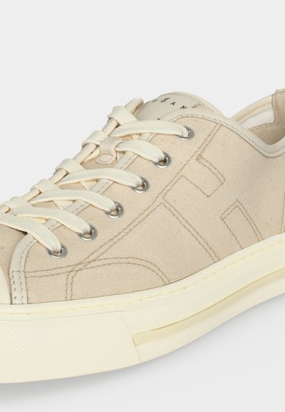 Μπεζ καμβάς αθλητικό παπούτσι χαμηλής κοπής με λευκά κορδόνια, μεταλλικά παπούτσια, ραμμένες λεπτομέρειες και χοντρή λαστιχένια σόλα σε εκρού χρώμα.