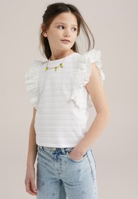 Bílý bavlněný top s rýhovanými rukávy, texturovaným designem a kulatým výstřihem, spárovaný s světle modrými džínami s výšivkami.