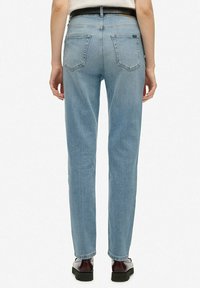 Jeans de pierna recta de color azul claro, hechos de mezclilla, con bolsillos traseros y cintura alta, combinados con un cinturón negro y zapatos marrones.