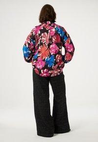 Bloemenschirt met levendige roze, blauwe en witte patronen op een zwarte achtergrond; losse pasvorm en lange mouwen in combinatie met gestructureerde zwarte broek.