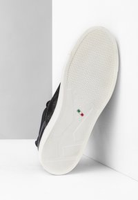 Musta mokkanahkasaapas valkoisella kumipohjalla, jossa on tekstuuripintoja ja brändäysdetaljeja. Koko 37, valmistettu Italiassa.