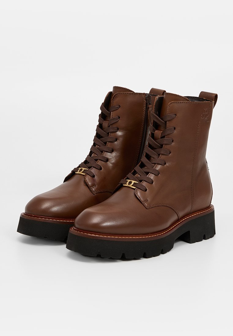 Braune Leder-Schnürstiefeletten mit einer auffälligen schwarzen Sohle, ausgestattet mit seitlichen Reißverschlüssen und goldfarbenen Hardware-Details. Glatte Textur, strapazierfähiges Design.