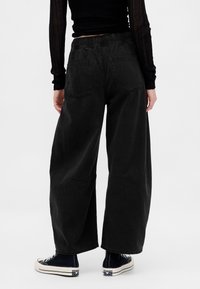 Jeans neri in denim a gamba larga con vita elastica, tasche posteriori e vestibilità ampia. Indossati con sneakers nere in tela.