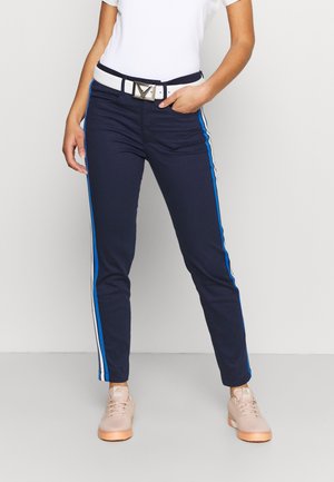 Pantalons slim-fit navy avec des rayures latérales blanches et bleues, associés à une ceinture blanche et des baskets rose clair. Mélange de coton avec une texture lisse.