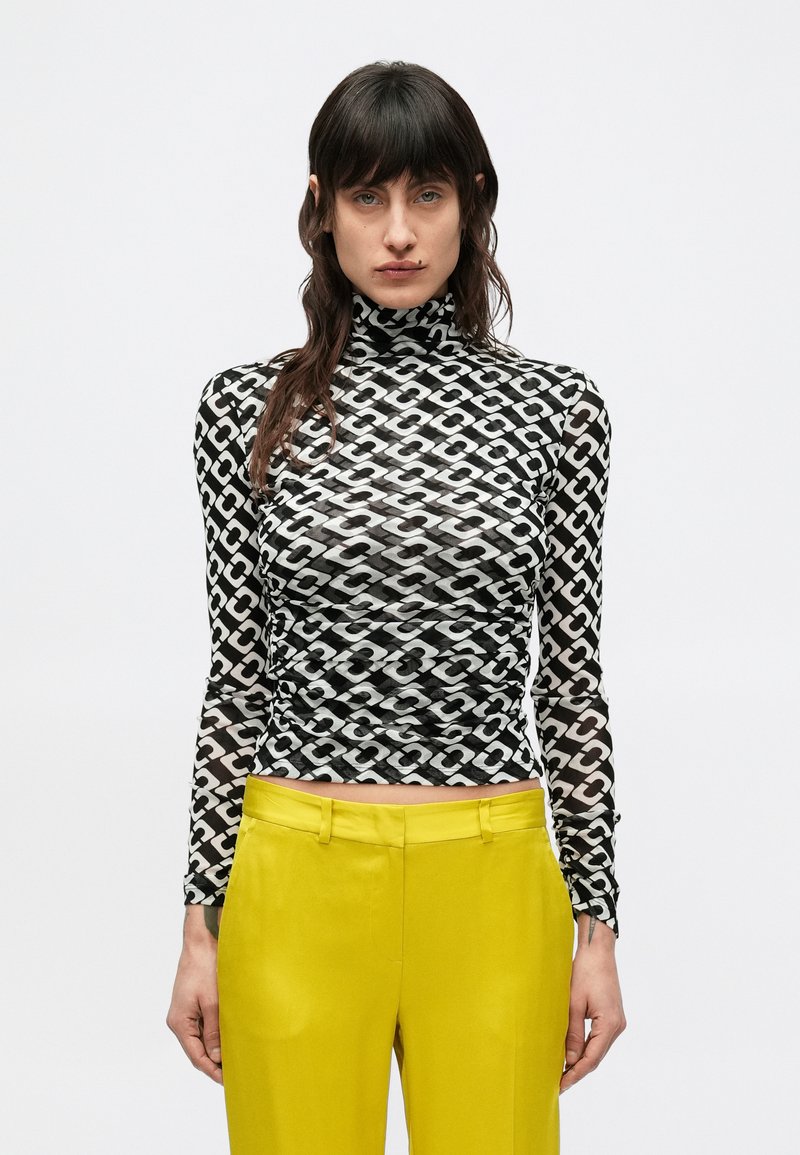 Čierno-biely rolák s dlhými rukávmi so vzorom, vyrobený z priesvitnej látky, v kombinácii so žltými vysokými nohavicami.