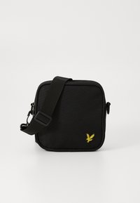 Zwarte schoudertas van een gestructureerde stof, vierkante vorm, verstelbare schouderband en een gele vogel logo geborduurd op de voorkant.