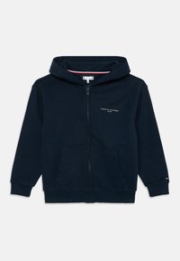 Mornarsko plava dukserica s patentnim zatvaračem, prednjim džepovima, rebrastim manžetama, malim Tommy Hilfiger logotipom na prsima i rukavu, te kapuljačom.