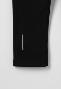 Pantalons de sport noirs en tissu extensible ; dotés d'une bande verticale réfléchissante argentée près de l'ourlet ; texture lisse, design fuselé.