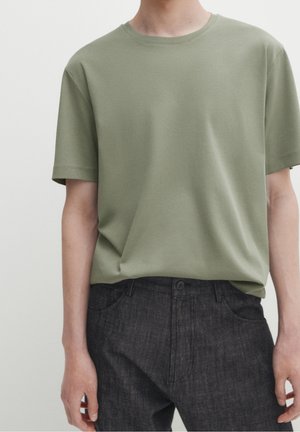 Olive green cotton t-shirt with a crew neckline and short sleeves, paired with dark denim pants featuring a button closure and side pockets.