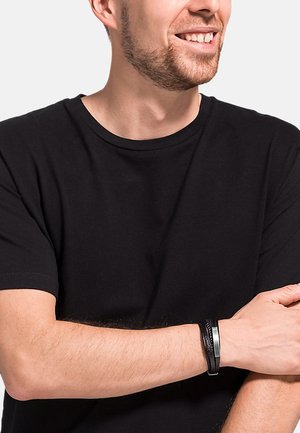 Black leather bracelet with a metal clasp, featuring a textured design, worn on a wrist with a black t-shirt in a neutral background.