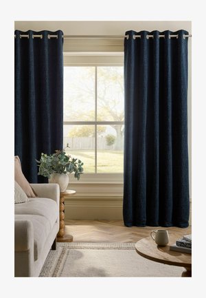 Großes Fenster, eingerahmt von dunkelblauen Vorhängen, mit einem beigen Sofa, einem runden Holztisch mit einer Blattpflanze und einem Couchtisch mit einer Tasse und Büchern.