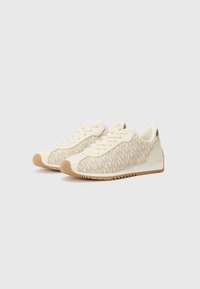 Sneakers med en overdel i cremefarvet stof, der har et gentaget logo mønster i tan, rund tå og en lys brun gummisål med zigzag mønster.