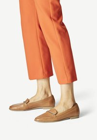 Mocassins en cuir tan avec un accent chaîne, semelle plate et bout rond, associés à un pantalon orange cropped au toucher doux.