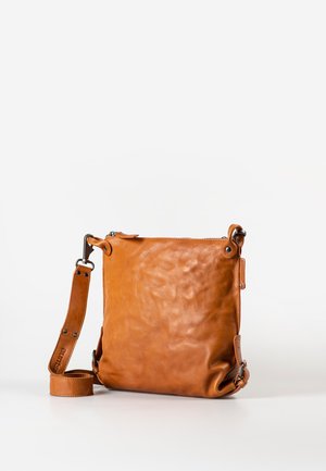 Bruine leren crossbodytas met verstelbare schouderriem, ritssluiting en metalen accenten, rechtopstaand op een witte ondergrond.