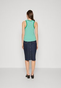 Top de tirantes finos a rayas verdes, combinado con una falda de mezclilla oscura ajustada que tiene un dobladillo sin terminar y bolsillos traseros. Zapatos de tacón cuadrado negros.