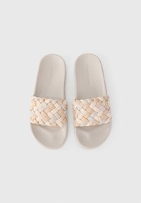 Υφασμένες παντόφλες σε μπεζ και κρέμ. Μαλακή, υφασμένη λωρίδα με πλεγμένο σχέδιο, επίπεδη σόλα και διακριτικό λογότυπο στο εσωτερικό.