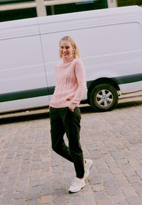 Light pink knitted turtleneck sweater with cable knit design, paired with black cargo pants and light sneakers on cobblestone pavement.