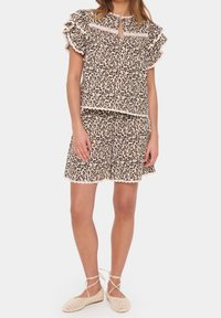 Koszulka z krótkim rękawem w panterkę i pasujące szorty, obie z falbaniastymi brzegami i kośćmi słoniowymi; lekką tkanina; casualowy krój; połączone z beżowymi butami.