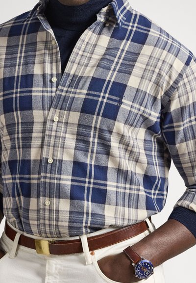 Rutete skjorte i marineblå og kremfarger, med knappet ned krage og mykt stoff. Brukes med brun belte og blå klokke.