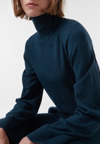 Pull en col roulé bleu marine en tissu doux et texturé. Manches longues avec des poignets côtelés. Design simple avec un minimum de détails.