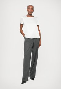 Blusa bianca a maniche corte abbinata a pantaloni grigi larghi. La blusa ha una trama liscia, mentre i pantaloni sono testurizzati con sottili motivi.