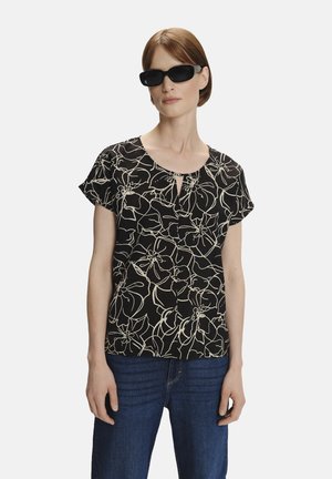 Top negro de manga corta con un patrón floral blanco y un detalle de escote en forma de llave, combinado con unos jeans de mezclilla azules.