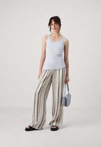 Lyseblå ribbet tanktop med bølget blondekant, sammen med brede stripete bukser i beige, grå og marineblå, og en grå håndveske.