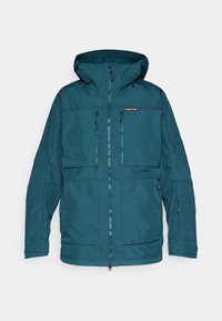 Veste imperméable teal avec capuche, fermeture éclair à l'avant et plusieurs poches zippées. Présente une texture douce et des poignets réglables.