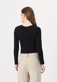 Black long-sleeve top with a round neckline, paired with light beige high-waisted pants, featuring rear pockets and a sleek fit.