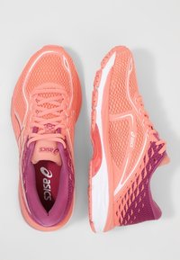 Scarpe da corsa con una tomaia in mesh rosa, dettagli bianchi e viola, una suola ammortizzata e intricati motivi laterali.