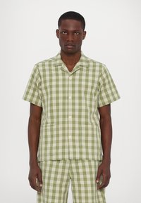 Κοντομάνικο πουκάμισο με πράσινο και λευκό καρό σχέδιο, με κερατοειδή γιακά, κουμπιά μπροστά και εξωτερικές τσέπες. Κατασκευασμένο από ελαφρύ υλικό.