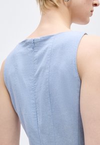 Κοντινό πλάνο ενός ατόμου που φοράει ένα αμάνικο γαλάζιο φόρεμα με φερμουάρ στην πλάτη, που δείχνει την περιοχή της άνω πλάτης και των ώμων.