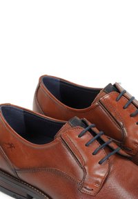 Zapatos de cuero marrón con una superficie texturizada, punta redonda y cordones azules. Presentan un acento negro en la lengüeta y una suela contrastante.