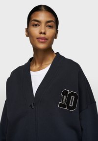 Marineblauer Cardigan mit Schalkragen, Ein-Knopf-Verschluss und gesticktem "10 DAYS"-Patch auf der linken Brust. Weicher, strukturiert Stoff.